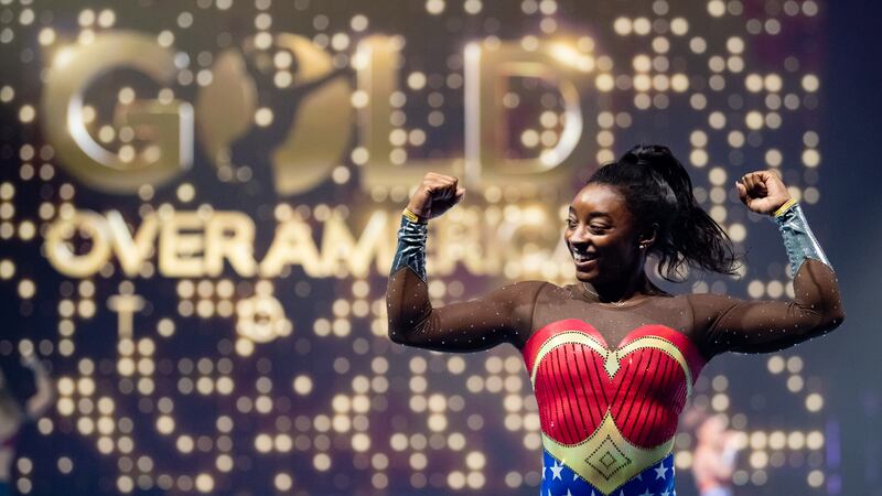 Simone Biles in superstar outfit in front of Gold Over America logo.
